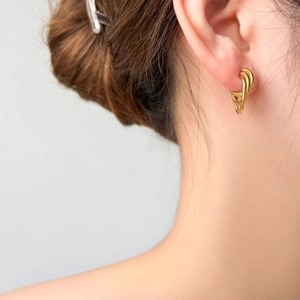 Close-up of triple-layered crossing curved gold earrings worn on a model's earlobe