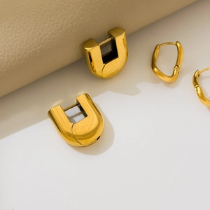 Macro view of gold U-shaped hoop earrings and textured rings with mirror finish