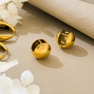 Detailed view of golden spherical huggie earrings on textured leather background