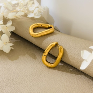 Close-up of geometric U-shaped hollow gold earrings on a premium beige leather background