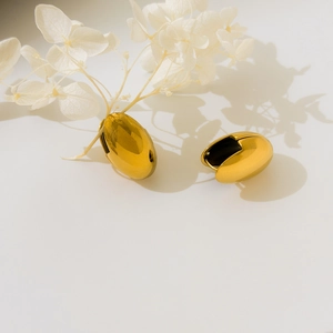 Detailed close-up of oval gold hoop earrings with mirror-polished metallic finish