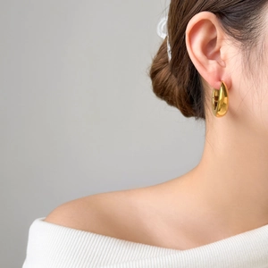Close-up of a wide polished gold hoop earring featuring a smooth curved U-shape on model