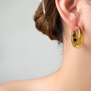 Close-up of chunky gold-plated U-shaped hoop earrings on a model showing high-polish texture