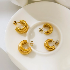 Détail de boucles d'oreilles créoles dorées 18K en forme de C sur un plateau en céramique
