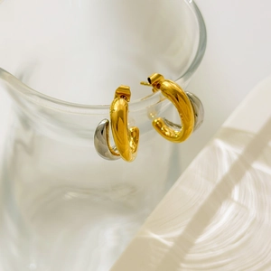Détail macro de boucles d'oreilles bicolores en forme de C en or et argent sur verre