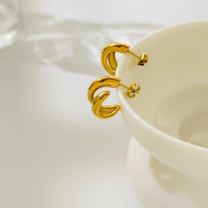 Détail de boucles d'oreilles créoles C dorées posées sur un bord de tasse blanche