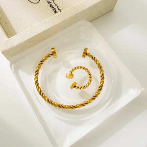 Close-up of golden twisted cable bracelet and matching open ring on a clear tray