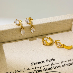 Golden earrings set with pear and square zircon charms on printed jewelry box