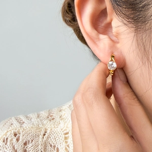 Close-up of golden hoop earring with round white zircon stone on female model ear