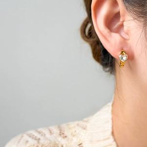 Detail of a 18K gold plated heart zircon earring worn by a model in a minimal setting