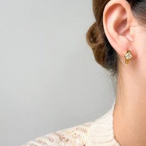 Close-up of golden square zircon earrings with a polished finish worn by a model