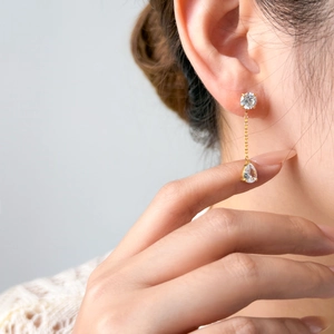 Close-up of a gold-plated tassel drop earring with pear-cut zircon worn on ear