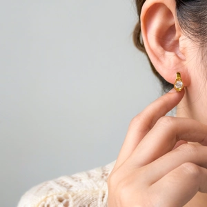 Detail of 18K gold plated teardrop earring with zircon stone worn by a model