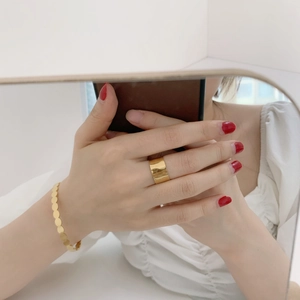 Detailed view of matte gold wide cuff ring and layered circular sequin bracelet on wrist