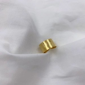 Minimalist wide gold-plated open ring with a smooth metallic texture on white linen