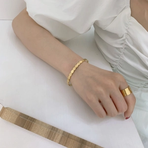 Detail of wide gold textured ring and chunky coin chain bracelet worn on model