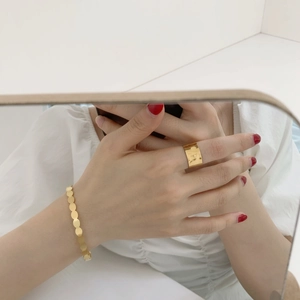 Detailed close-up of golden circle-link bracelet and wide band ring on reflective surface