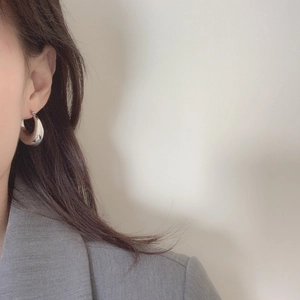 Close-up of a minimalist silver U-shaped hoop earring on a model wearing a grey blazer