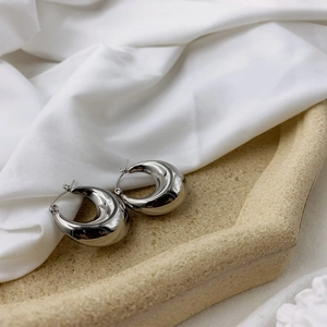 Detailed view of polished silver U-shaped hoop earrings on elegant silk fabric