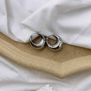 Detailed view of silver thick hoop earrings with polished finish on soft fabric background