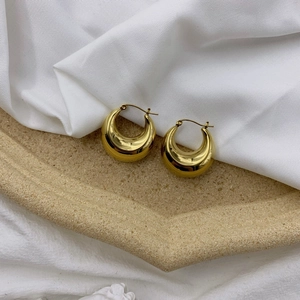 Close-up of golden teardrop hoop earrings with a mirror-polished finish on stone tray