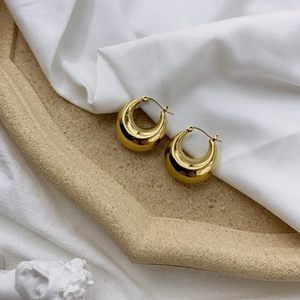 Close-up of elegant gold hoop earrings on a textured stone tray and white fabric