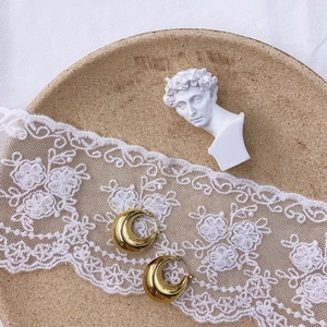Detailed close-up of golden croissant hoop earrings on a vintage lace background