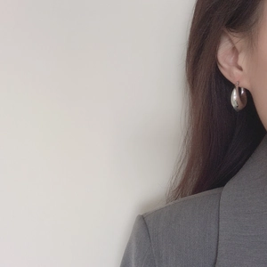 Close-up of minimalist silver water drop hoop earring worn with a professional grey blazer
