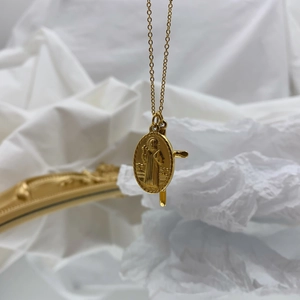 Collier en or avec pendentif ovale Vierge Marie et croix sur tissu texturé blanc
