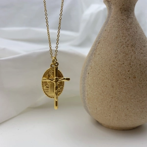 Collier doré avec médaille de la Vierge Marie et pendentif croix sur un vase beige