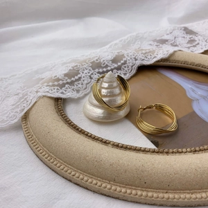 Detail of layered gold hoop earrings on decorative white shell and lace background