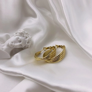 Elegant multi-layered gold wavy hoop earrings on a white silk background with a plaster statue