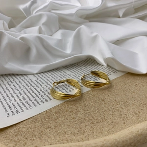 Detail shot of multi-layer intertwined gold hoop earrings on a vintage paper background