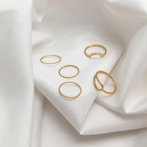 Set of 5 minimalist gold rings in various bohemian styles on white satin background