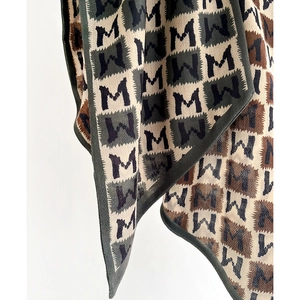 Checkered knit scarf with M letter pattern in beige and brown, showing soft drape