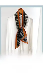 Detail of narrow silk scarf with houndstooth pattern and orange border on white shirt