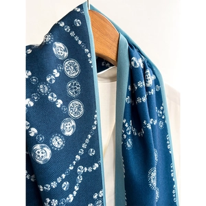 Blue herringbone silk scarf with vintage button prints hanging on a wooden hanger