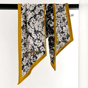 Floral print skinny silk scarf with yellow borders hanging on a minimal black bar