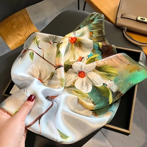 Floral print silk square scarf in blue and green draped over a luxury leather handbag