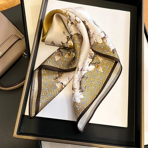 Carré de soie doré élégant aux motifs floraux présenté sur un plateau blanc de luxe