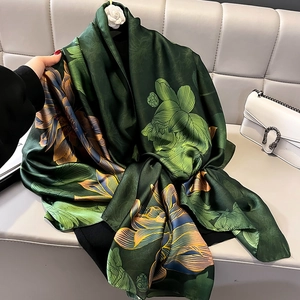 Eleganter dunkelgrüner Seidenschal mit Lotusblumenmuster auf grauem Sofa liegend