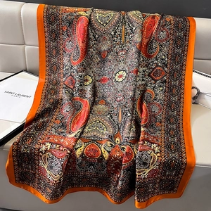 Large silk scarf with orange borders and paisley patterns draped on white leather furniture