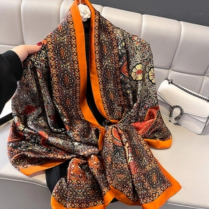 Large paisley print silk shawl in warm tones draped elegantly on a white sofa