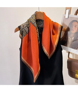 Dettaglio della sciarpa di seta con motivi geometrici arancio e verdi su top nero