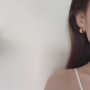 Close-up of a high-polished gold geometric round earring worn on a female ear