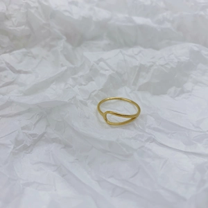 Close-up of minimalist gold teardrop cutout ring on textured white paper background