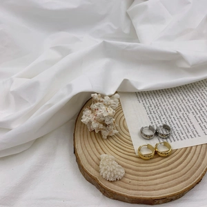 Detail of gold and silver irregular round hoop earrings on a minimalist wooden display