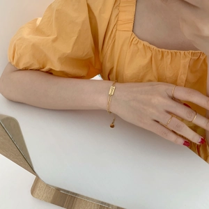 Minimalist gold rings and Lucky engraved chain bracelet worn on hand with orange sleeve