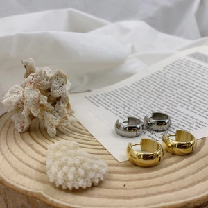 Irregular chunky huggie hoop earrings in polished gold and silver on a wooden tray