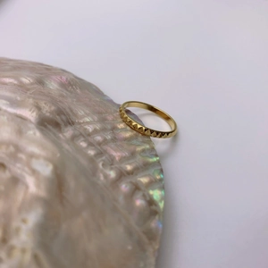 Minimalist gold plated ring with geometric rivet pattern on an iridescent shell background